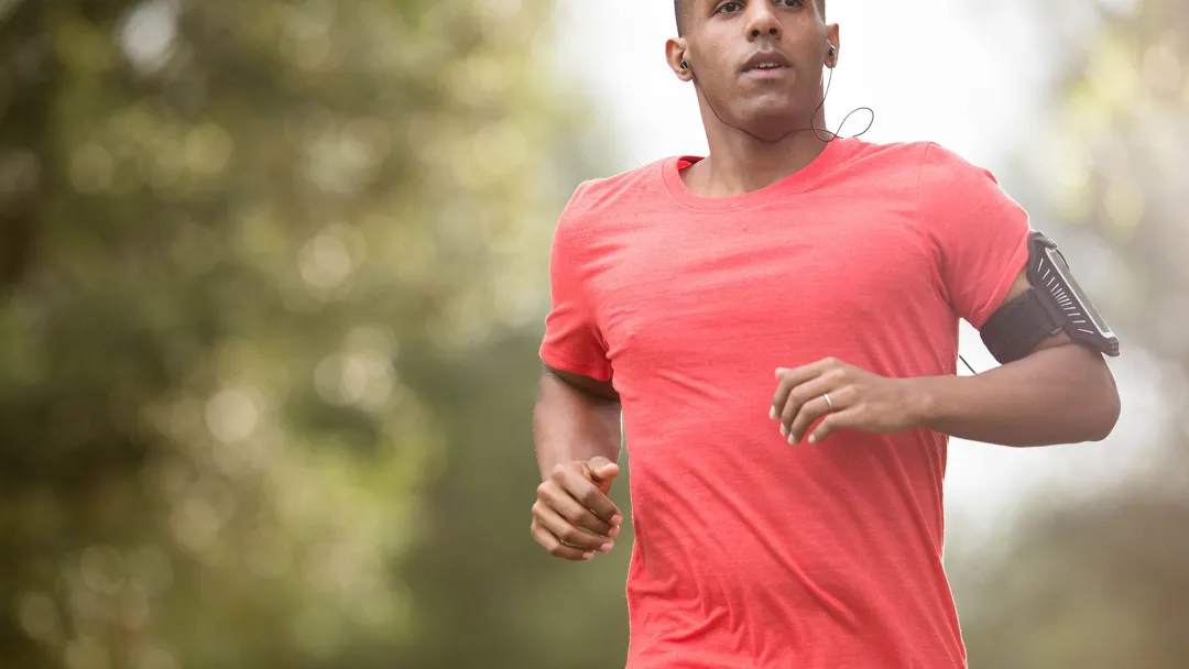 Man in a red shirt running outside while listening to music.