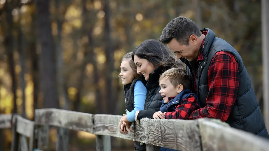 A family of four leaning on a fence while outdoors in the winter.