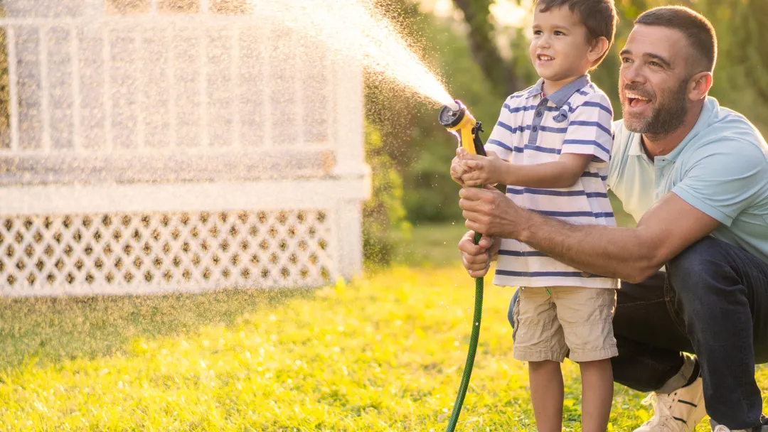 A Father and Son Spray a Garden Hose in the Front Yard as They Laugh
