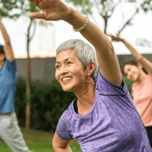 A Senior Woman Does Group Yoga in a Park