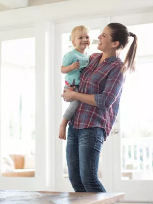 A mom holds her toddler son in a living room full of toys