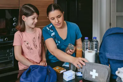 A Mother Looks Over a First Aid Kit with Her Daughter on the Kitchen Table.