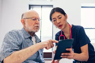 An older man looks at a tablet with a nurse.