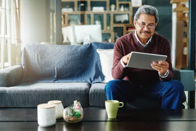 Senior man checking iPad while sitting on a couch while at home.