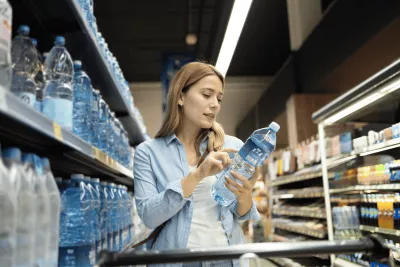 Woman looking at a water bottle at a grocery store.