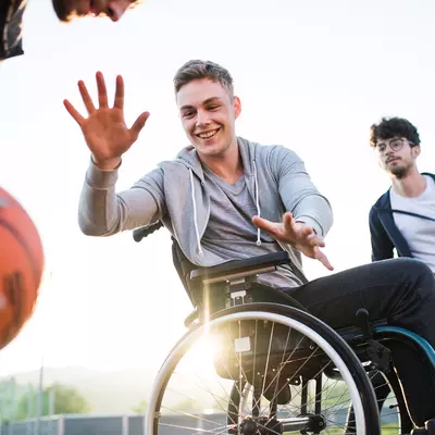 Older teens playing basketball one of which is in a wheelchair 