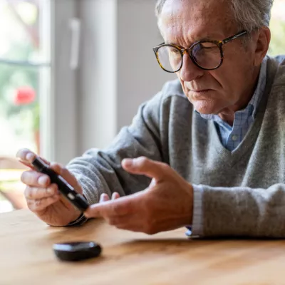 A Senior Checks His Glucose Levels with a Device While Sitting at the Kitchen Table
