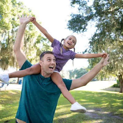 A Father Carries His Daughter on His Shoulders as they Play in a Park