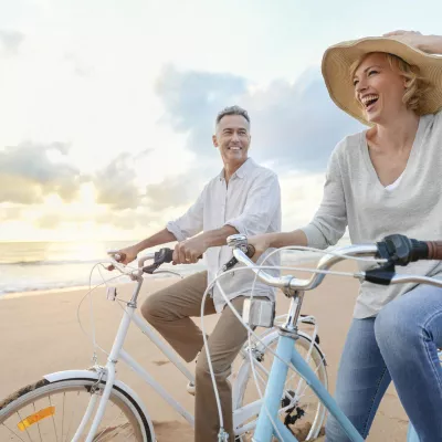 Man and woman in a hat riding bicycles on the beach at sunset.