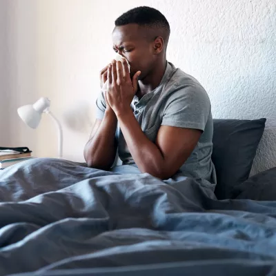 A man sneezing in bed. 