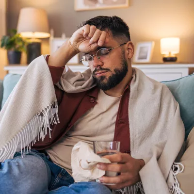 Man sitting at home on the couch wrapped in a blanket while sick with the flu.