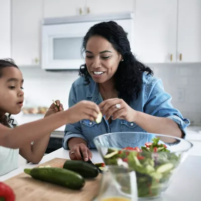 A mother and daughter prepare a salad at home.