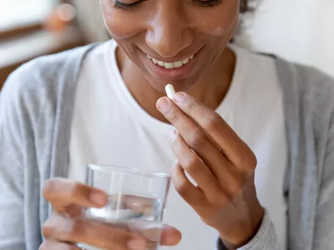 A woman smiles as she's about to take a vitamin.