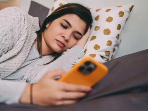 A Woman Lays on a Bed Looking at Her Cell Phone.