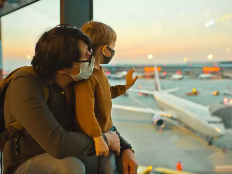 Father and son watch planes at the airport before boarding wearing face masks