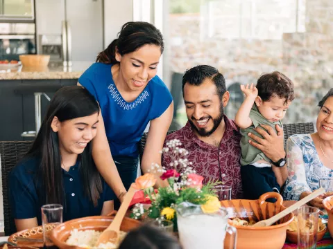 A Hispanic Family Sits Down to a Meal in Their Home.