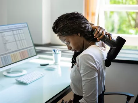 A woman using a massage gun on her back