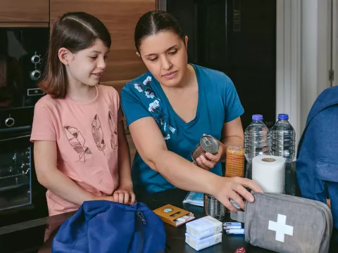 A Mother Looks Over a First Aid Kit with Her Daughter on the Kitchen Table.