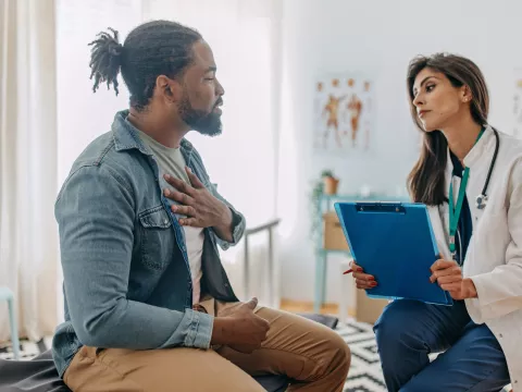 A Patient Holds His Hand to His Chest as He Consults with His Physician in a Doctor's Office.