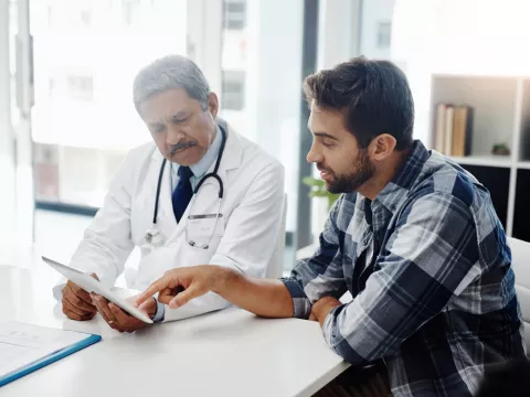 A Doctor Reviews a Patient's Chart with Him on a Tablet in His Office.