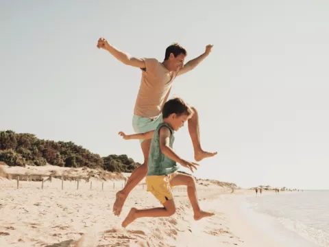 A Father and Son Jump Off a Dune on the Beach