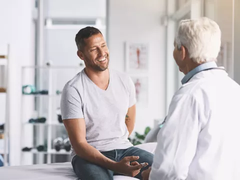 A Man Smiles as He Speaks to His Provider in an Exam Room