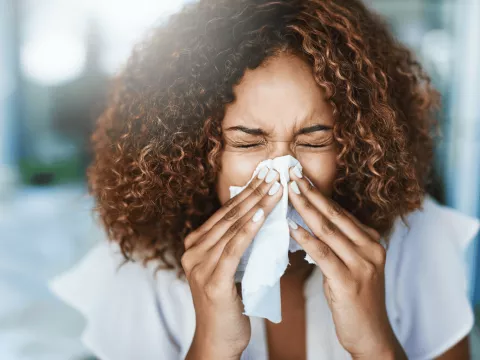A Woman Sneezes into a Tissue at Home