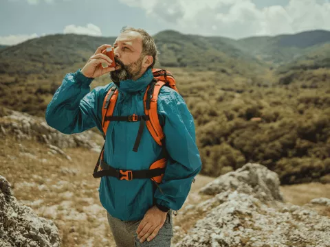 A Man Uses a Inhaler on a Hike Through Rough Terrain