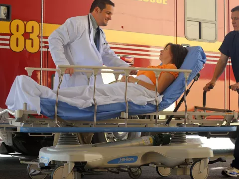 Woman arriving in a stretcher from ambulance with a doctor by her side.