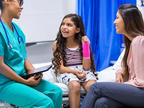 Child with a cast on her arm is sitting with a doctor and her mother