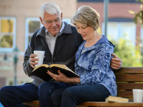Elderly Couple sitting on a park bench reading the Bible.