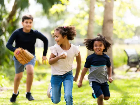 Three Hispanic Children Play Baseball in a Park
