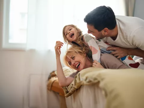 A mother and father play with their child in a bedroom.