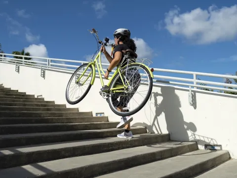 A woman running up a flight of stairs carrying a bicycle in her arms.