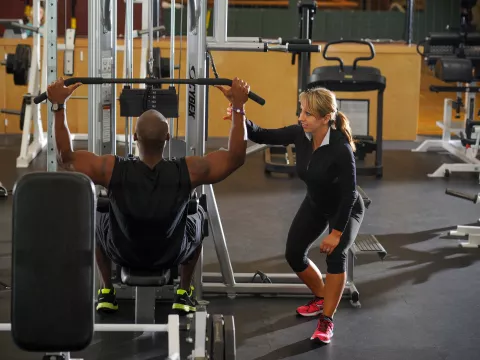 Female personal trainer coaching male trainee with a lat pulldown exercise.