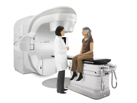 Oncologist with a female patient sitting on the bed of the TrueBeam Radiotherapy System from Varian Medical Systems.