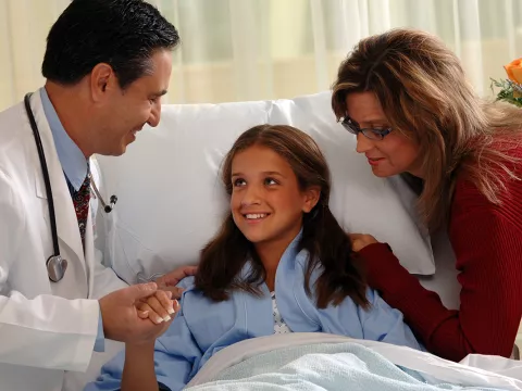 A young patient with her mom holds the hand of her doctor.