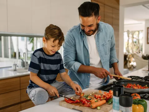 A father an son laugh together while preparing a healthy meal.