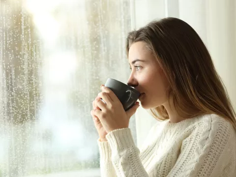 A woman drinking indoors while looking through the window