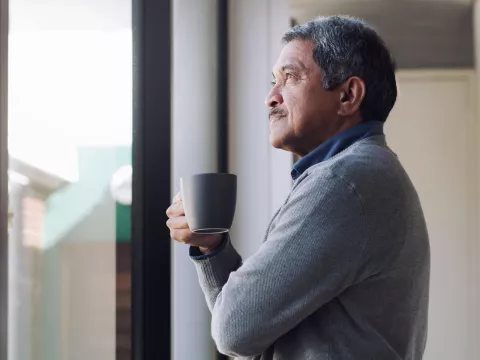 A man drinking coffee while looking outside from his window