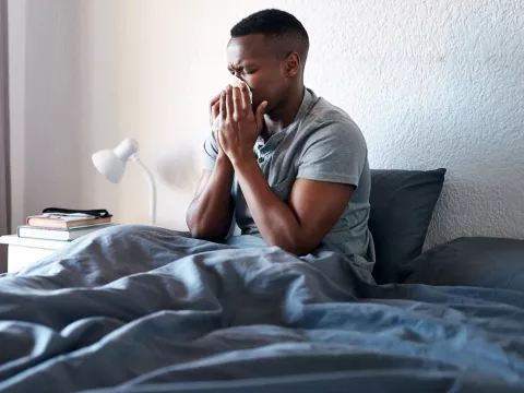 A man sneezing in bed. 