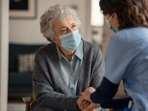 Hospice worker in mask, talking to elderly patient