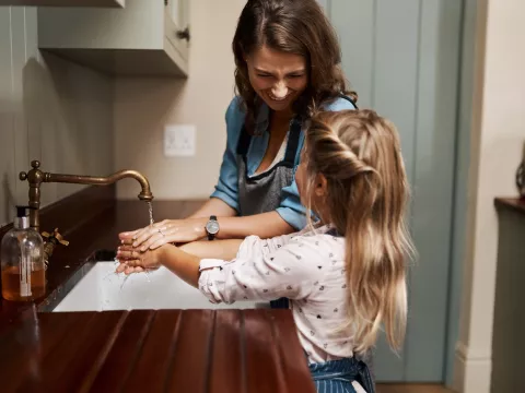 A mother and daughter wash their hands at the kitchen sink.