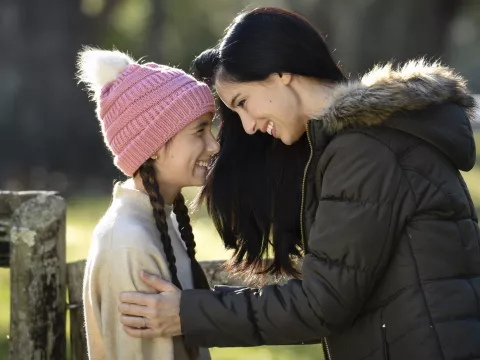 A mother and daughter smiling while outdoors.