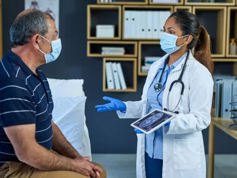 A masked doctor talking to her masked patient with a tablet on her hand