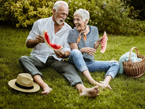 A couple eating watermelon at an outdoor picnic.