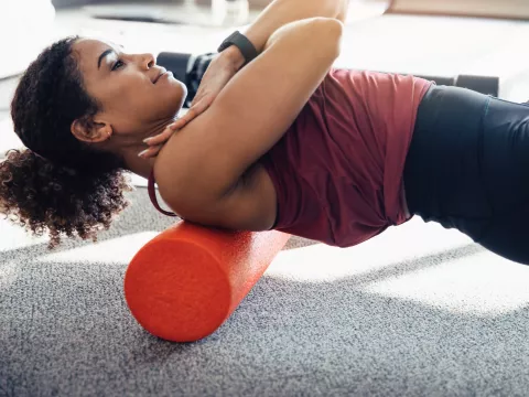 A woman foam rolling her upper back.