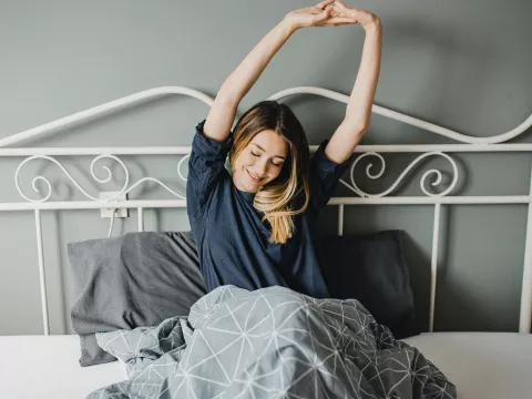A woman stretching in bed after a good night's sleep.