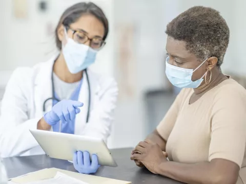 Doctor talking with patient about results on tablet, wearing masks