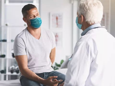 Man talking with doctor while both are wearing masks.